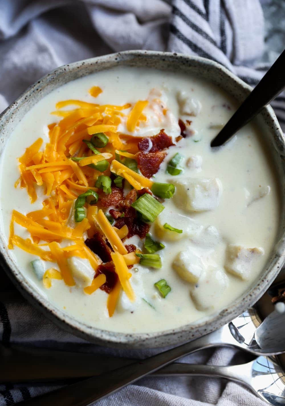 Bowl of potato soup with cheese and green onions.