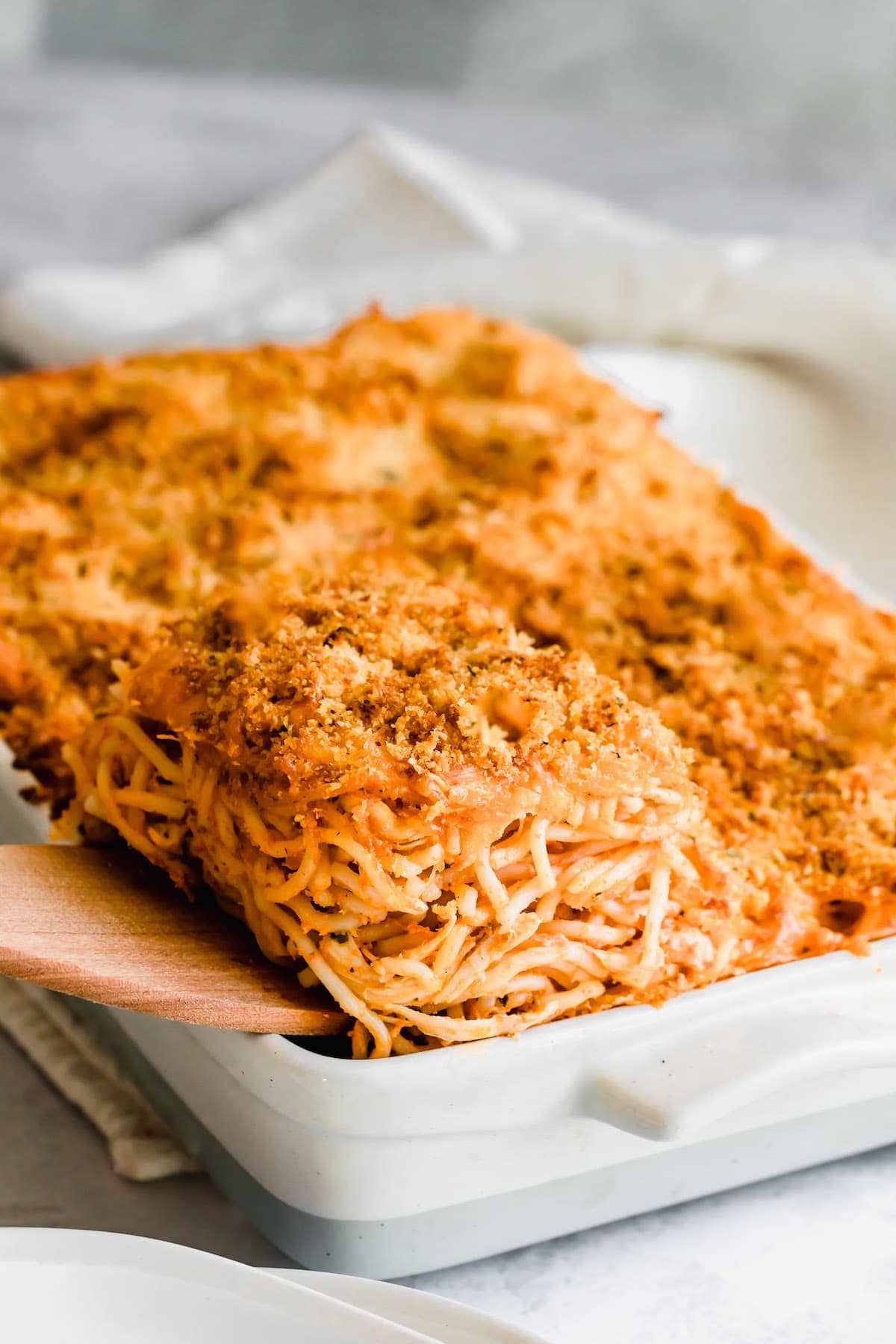 A wooden spatula lifts a serving of chicken spaghetti casserole from a baking dish.