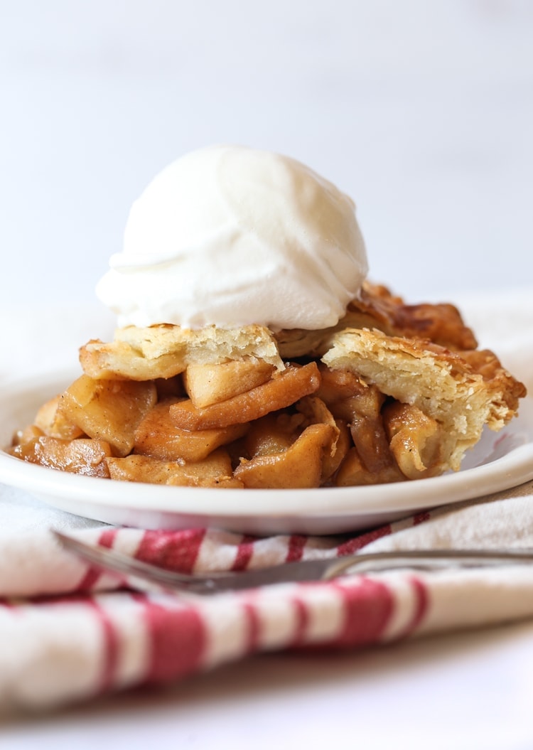 Apple pie slice topped with ice cream on a plate.