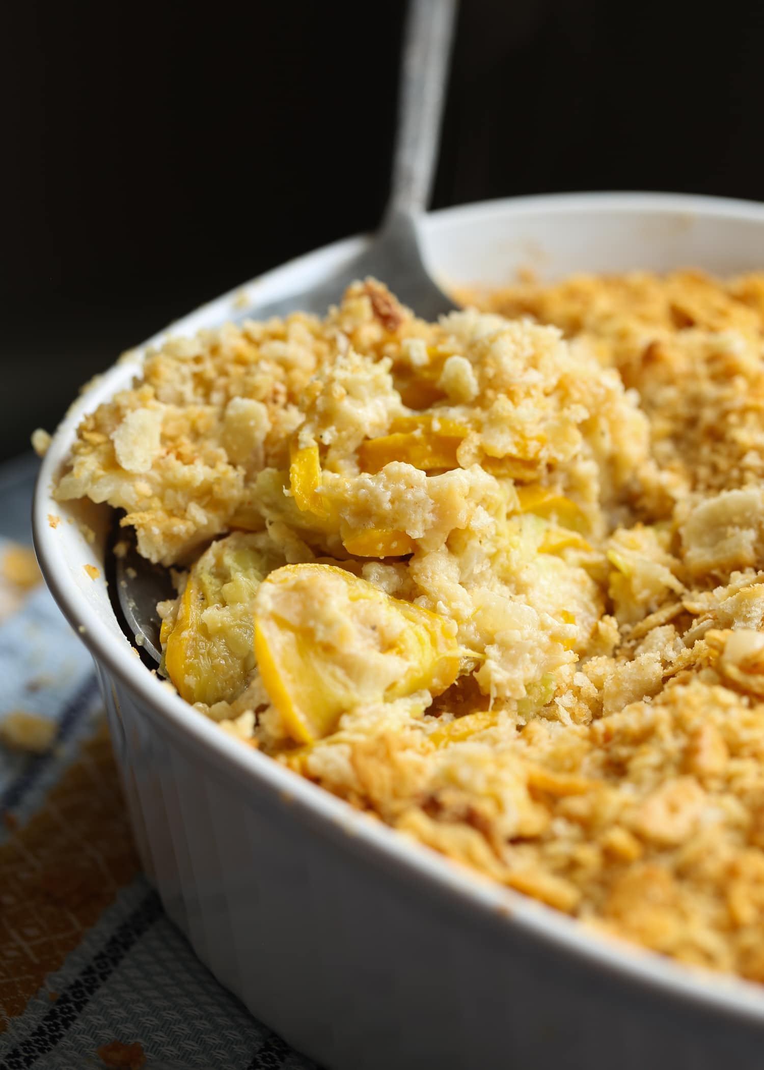 Ceamy squash casserole topped with crushed Ritz crackers in a baking dish with a serving spoon.