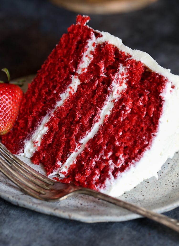 a slice of three layer red velvet cake with frosting